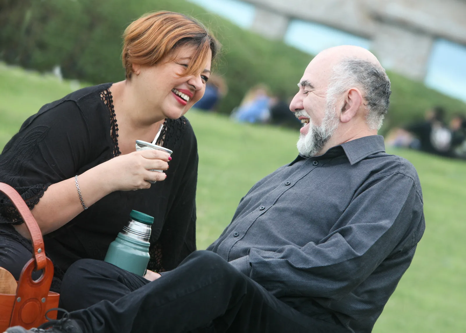 A woman and a man are laughing while sitting on the grass outdoors