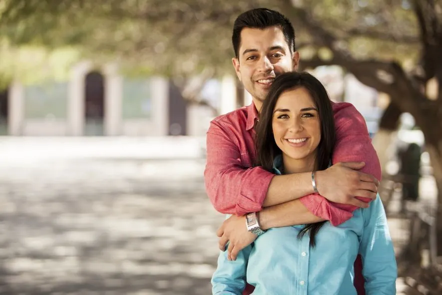 A young couple smiling, the man's arms around the woman's shoulders