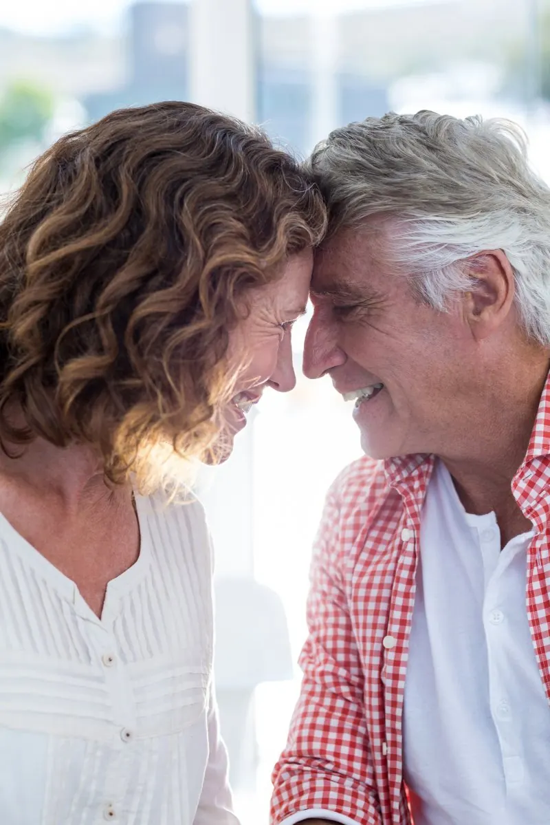 A mature couple with foreheads touching, smiling in a tender moment